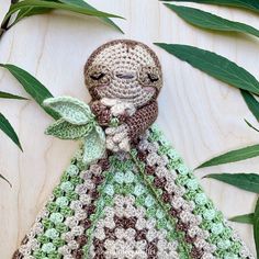 a crocheted stuffed animal is sitting on a table next to some green leaves