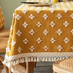 a yellow table cloth with white flowers on it and two wooden chairs in the background