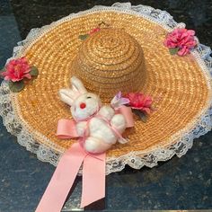 a straw hat with a pink ribbon around it and a stuffed bunny on top of it