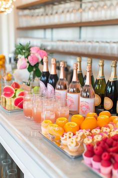 an assortment of drinks and snacks on a bar with flowers in vases behind it