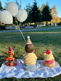 a small child sitting on a blanket with balloons in the shape of winnie the pooh and tigger