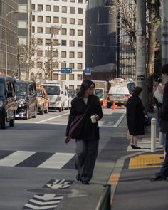 a woman walking across a street next to tall buildings