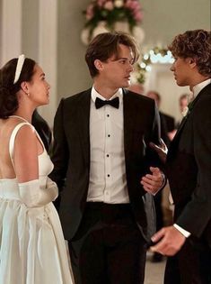 two men in tuxedos standing next to each other and one woman wearing a white dress