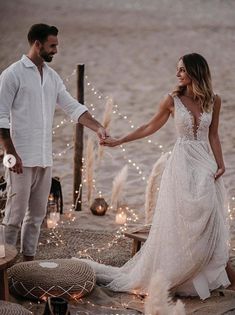 a bride and groom holding hands on the beach with lights in the sand behind them