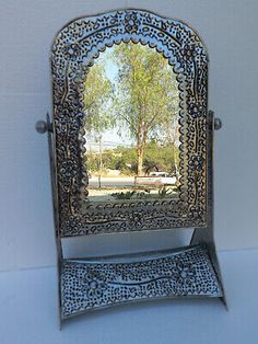 an ornate metal mirror on a stand with a tree in the middle and blue sky behind it