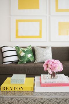 a coffee table topped with books and a vase filled with flowers next to a couch