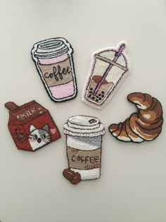 four embroidered patches with coffee, milkshake, and donut on them sitting on a white surface