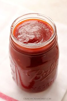 a glass jar filled with red liquid sitting on top of a white table cloth next to a spoon