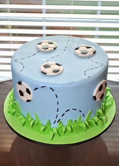 a blue cake with soccer balls on it sitting on a table next to a window