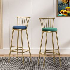 two golden barstools with blue upholstered cushions in front of a painting