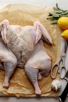 a raw chicken on a piece of paper next to some lemons and knifes