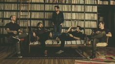 four men sitting on a couch in front of a bookshelf full of books