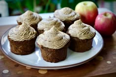 several cupcakes with frosting on a plate next to an apple