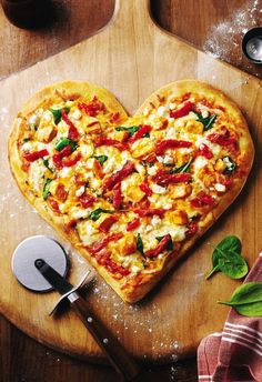 a heart shaped pizza sitting on top of a cutting board