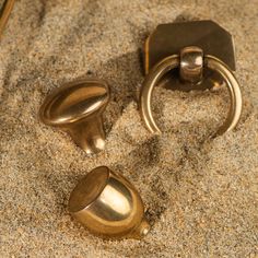 two brass door knobs are in the sand and one has a ring on it