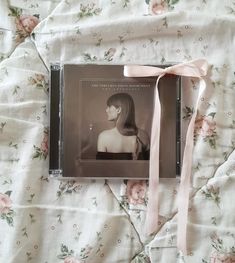 a cd with a pink ribbon on it laying on top of a floral bed sheet