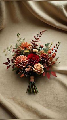 a bouquet of flowers sitting on top of a white cloth covered tablecloth with red, orange and green leaves