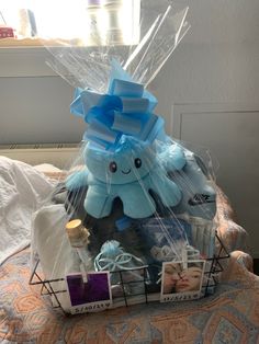 a blue stuffed animal sitting on top of a bed next to a basket filled with baby items