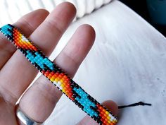 a hand holding a colorful beaded bracelet on it's thumb and the end of its string