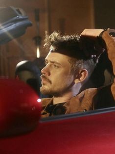 a man sitting in a red car with his hand on his head and looking out the window