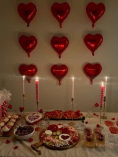 valentine's day dessert table with heart shaped balloons and candles on the wall behind it