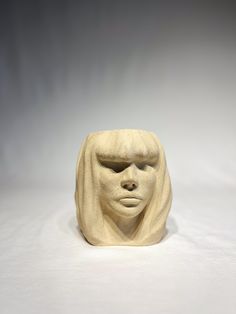 a white ceramic sculpture with a face on it's head and hair blowing in the wind