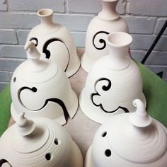 four white vases sitting on top of a green table next to a brick wall