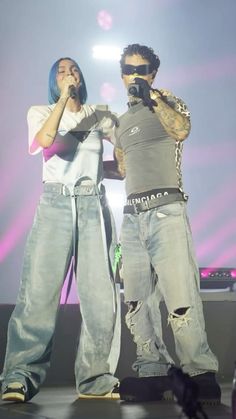 two people standing on stage with microphones in their hands and one person holding his head up