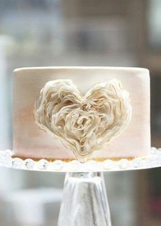 a heart - shaped frosted cake on top of a glass stand with an acrylic decoration