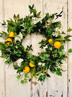 a wreath with oranges and white flowers hanging on a wooden wall, surrounded by greenery