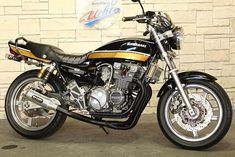 a black and gold motorcycle parked in front of a brick wall with a logo on it