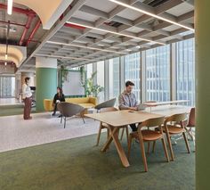 two people sitting at a table in an office with large windows and green carpeted flooring