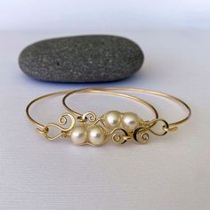 three bracelets with pearls on them sitting next to a rock