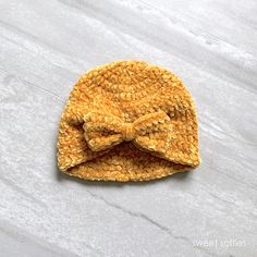 a small yellow hat with a bow on the front sitting on top of a white surface