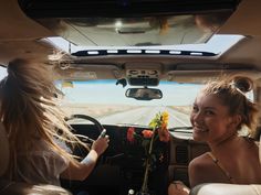 two women sitting in the back seat of a car with flowers on the dash board