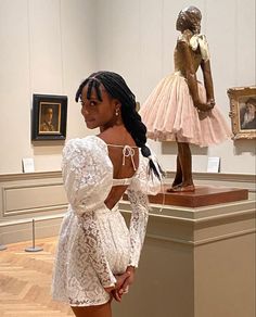 a woman standing next to a statue in a museum wearing a white dress and high heels