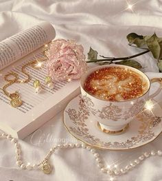 a cup of coffee on a saucer next to an open book and necklaces