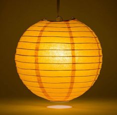 a large yellow paper lantern hanging from a ceiling fixture with dim lighting on the bottom