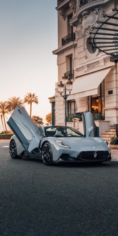 a silver sports car parked in front of a building with its doors open on the street