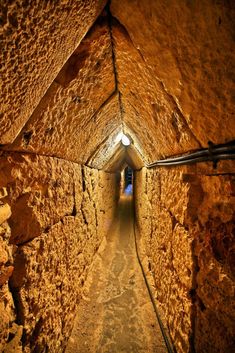 a narrow tunnel in the middle of a stone wall with light coming from it's end