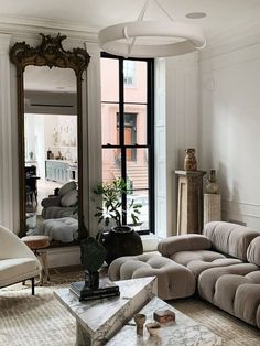 a living room filled with furniture and a large mirror on top of a wall next to a window