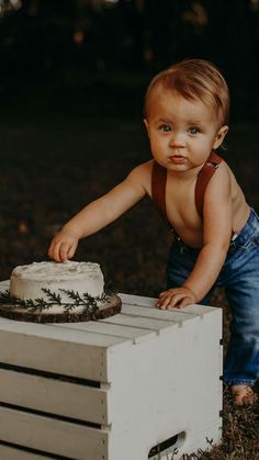 a baby standing next to a cake on top of a wooden crate in the grass