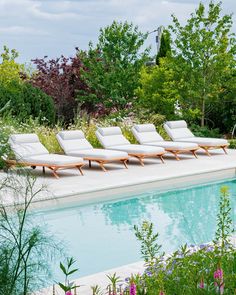 four lounge chairs sitting next to a pool in the middle of a lush green garden