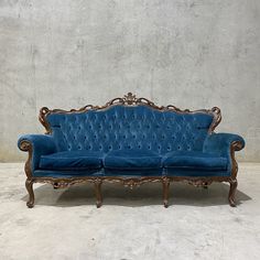 a blue velvet couch sitting on top of a cement floor next to a white wall