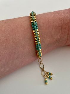 a woman's arm wearing a bracelet with gold beads and turquoise beads on it