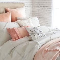 a bed with pink and white pillows on top of it, next to a brick wall