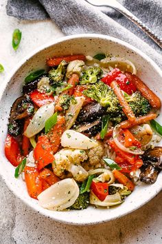 a white bowl filled with vegetables on top of a gray table next to a fork