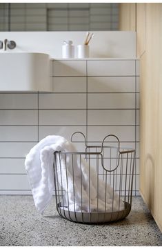 a metal basket with towels in it on the floor next to a sink and counter