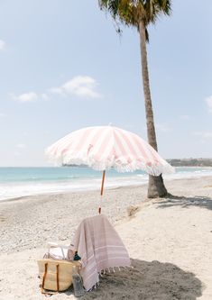 an umbrella and blanket on the beach with palm trees in the foreground, under a clear blue sky