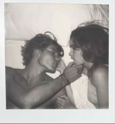 a man and woman laying in bed with one holding the other's hand to his mouth